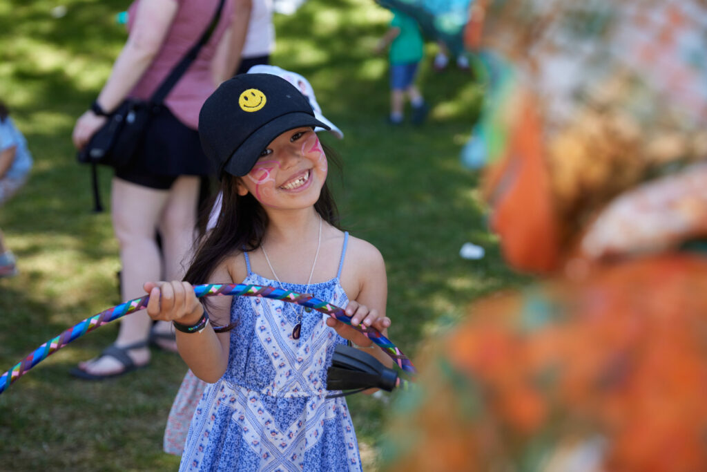A girl with face paint holding a hula hoop.